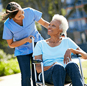 caregiver walking with an elderly woman in wheel chair